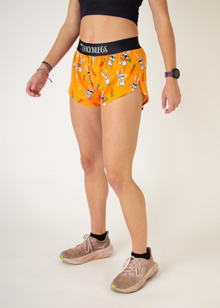 Runner is wearing ChicknLegs in the women's 1.5 in split running shorts with the bad bunny design. The print has white bunnys on it with sunglasses and orange carrots. 
