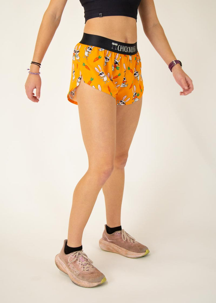 Runner is wearing ChicknLegs in the women's 1.5 in split running shorts with the bad bunny design. The print has white rabbit on it with sunglasses and carrot on an orange background.