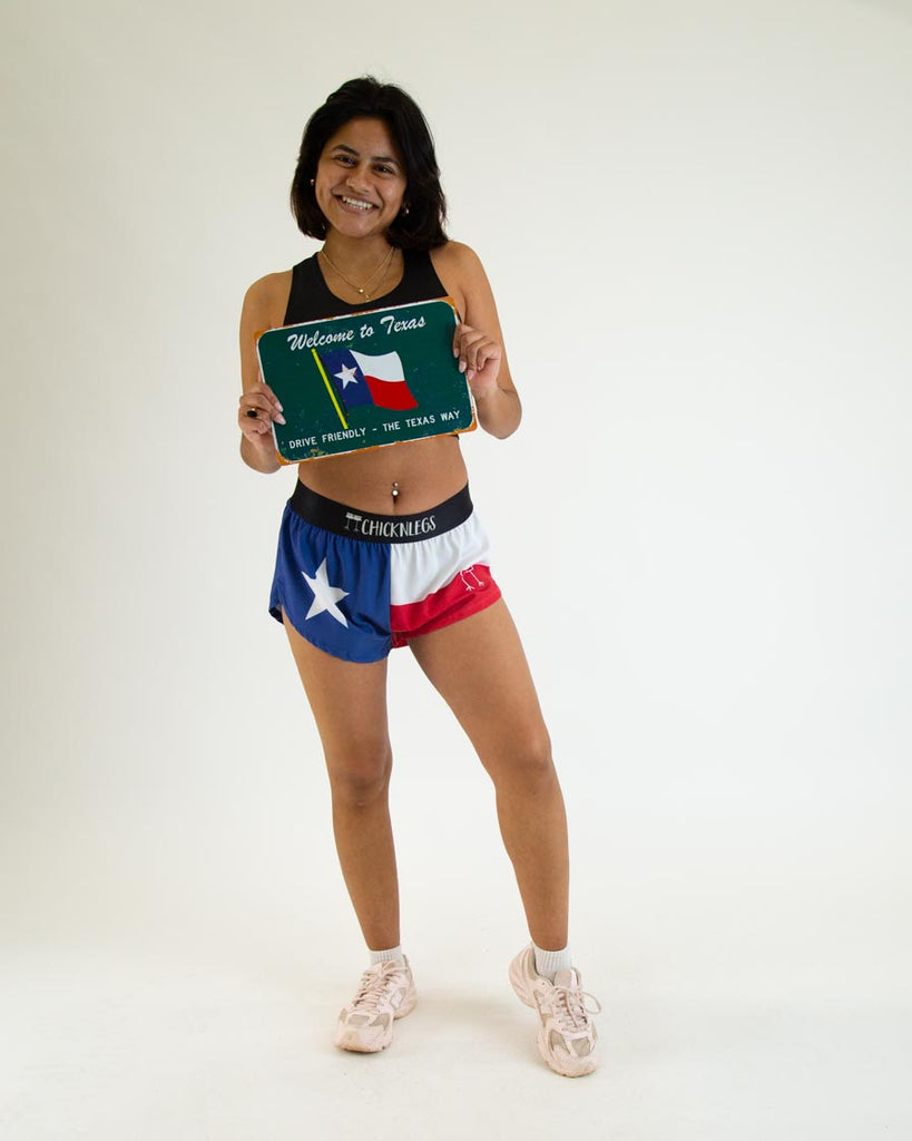 Runner is wearing ChicknLegs in the women's 1.5 in split running shorts in the texas flag print. The runner is holding a texas state flag plate.