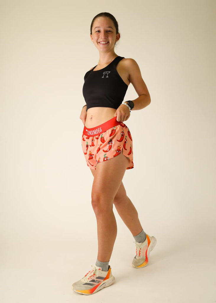 Model is wearing Chicknlegs women's 1.5 inch split running shorts in the chase pack chili pepper design, facing front while posing with the shorts.