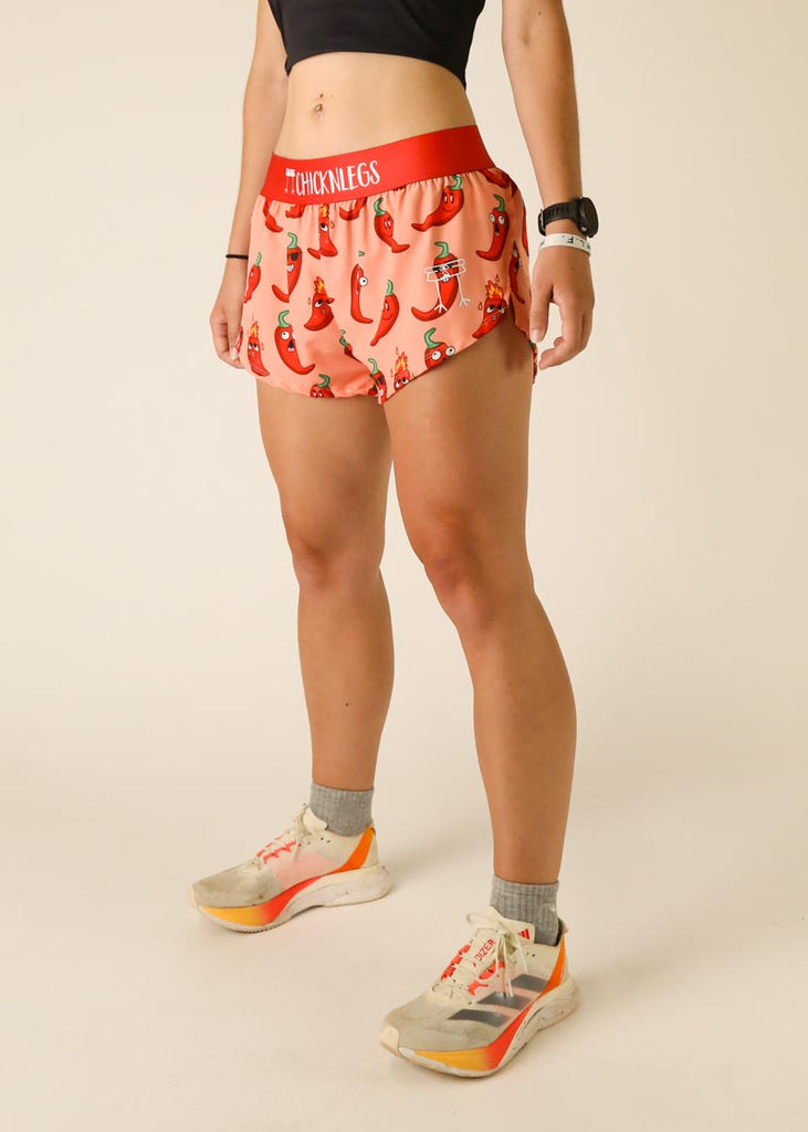 Model is wearing Chicknlegs women's 1.5 inch split running shorts in the chase pack chili pepper design, facing left.