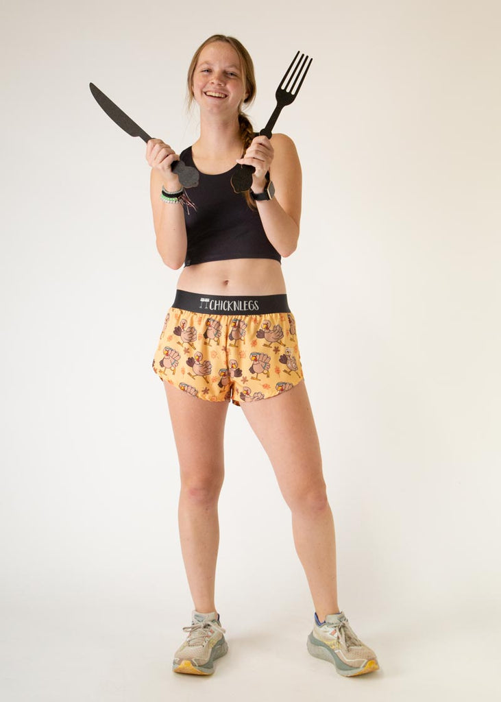The model is a runner who is wearing Chicknlegs women's 1.5" split running shorts in the pardoned turkey design, facing front while posing with a fork and a knife.