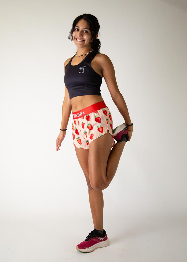 Model is a runner wearing Chicknlegs womens 1.5 inch split running shorts in the strawberry szn design, posing while stretching her back leg.