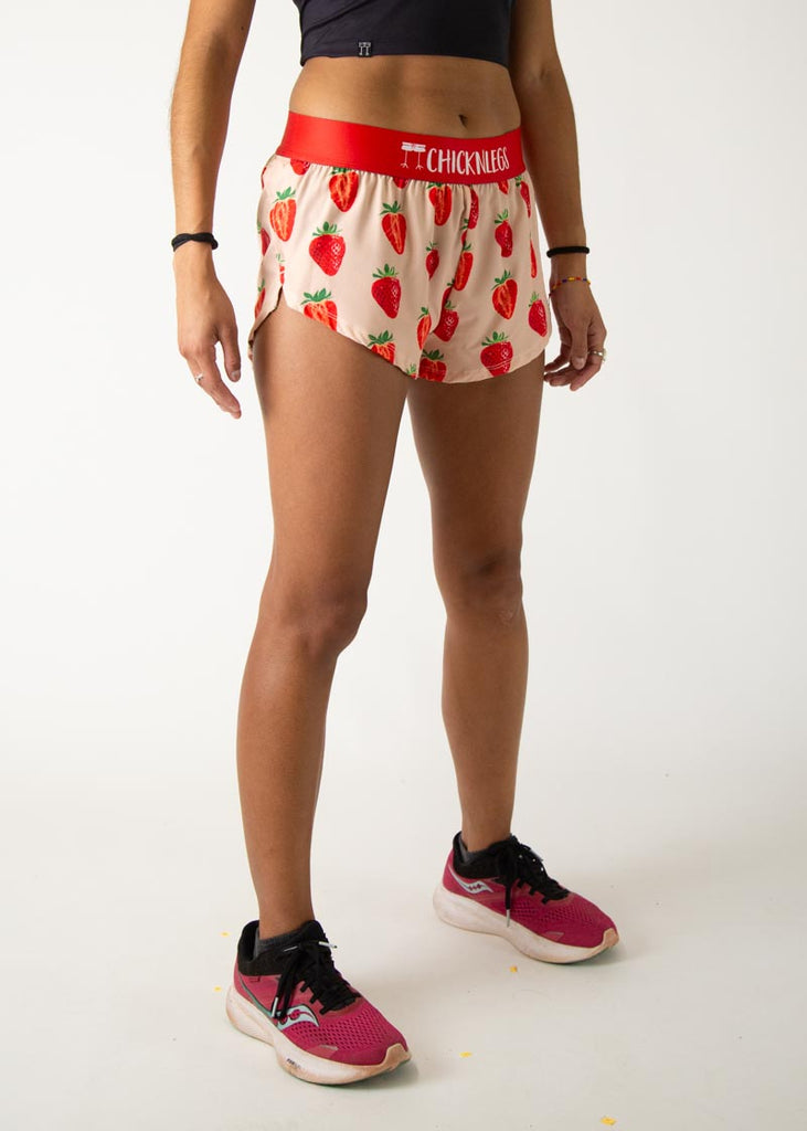 Model is a runner wearing Chicknlegs womens 1.5 inch split running shorts in the strawberry szn design, facing right.