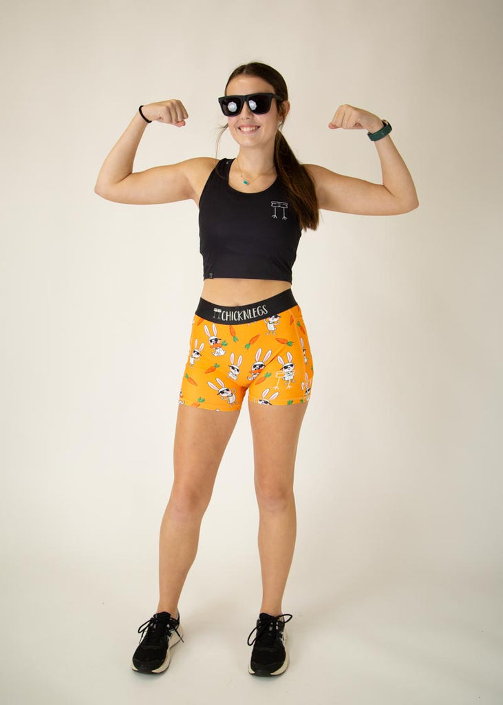 Runner is wearing ChicknLegs in the women's compression spandex in the bad bunny design, facing front. The print has white bunnys on it with sunglasses and carrots. The model is posing and flexing their muscles to match the bunnies.