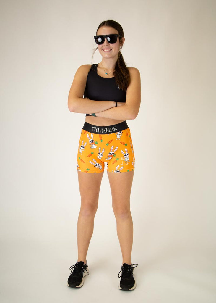 Runner is wearing ChicknLegs in the women's compression spandex in the bad bunny design, facing front. The print has white hares on it with sunglasses and carrots on an orange background.