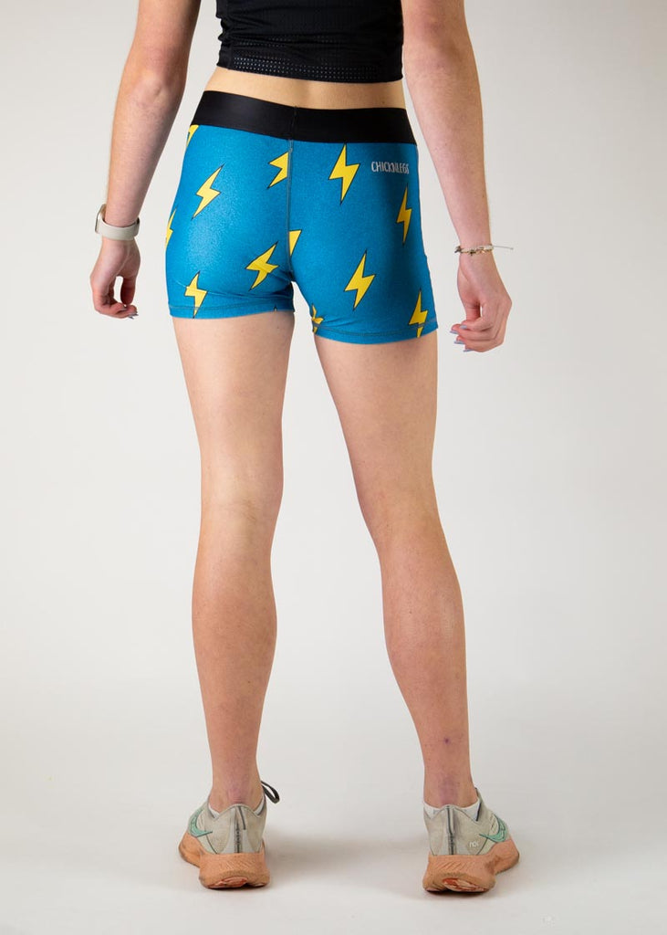 The model is a runner who is wearing Chicknlegs in the women's 3" compression shorts in the blue bolts design, facing away from the camera to show the back of the compression.