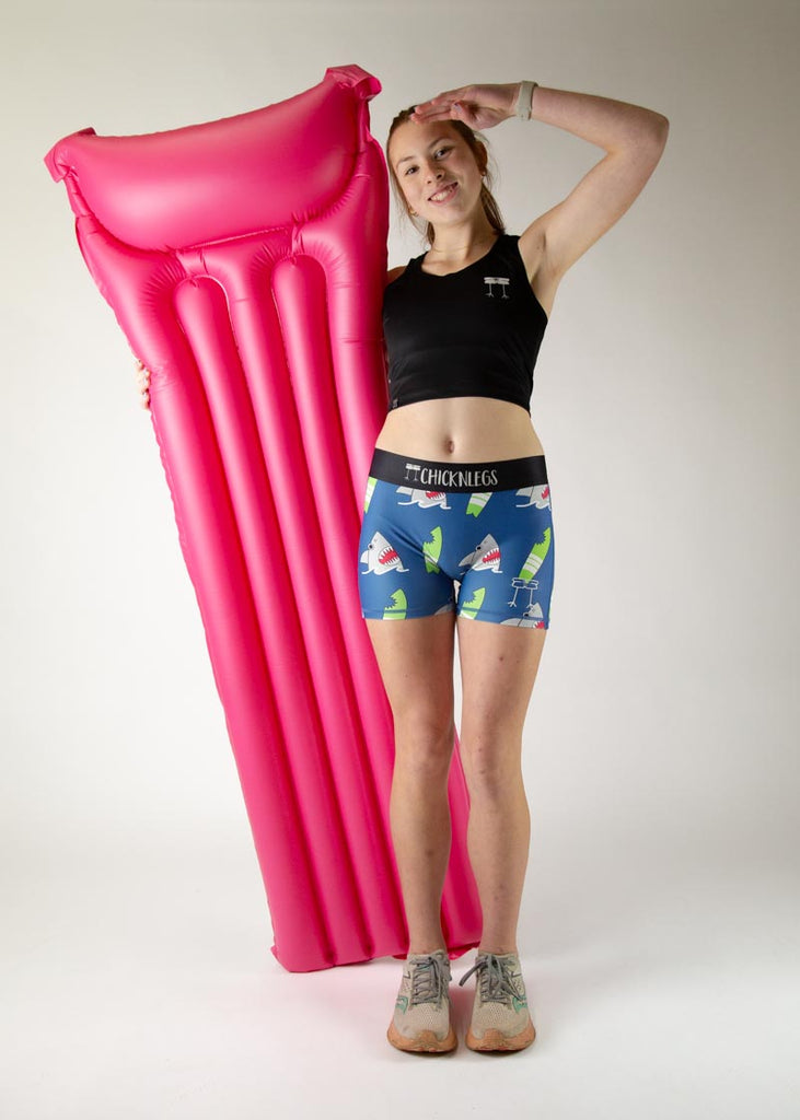 The model is a runner who is wearing Chicknlegs in women's 3" compression shorts in the blue sharks design, facing front while posing with a giant raft.