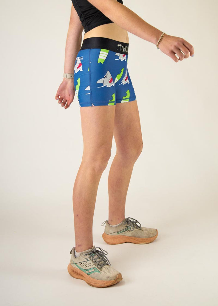 The model is a runner who is wearing Chicknlegs in women's 3" compression shorts in the blue sharks design, facing right.