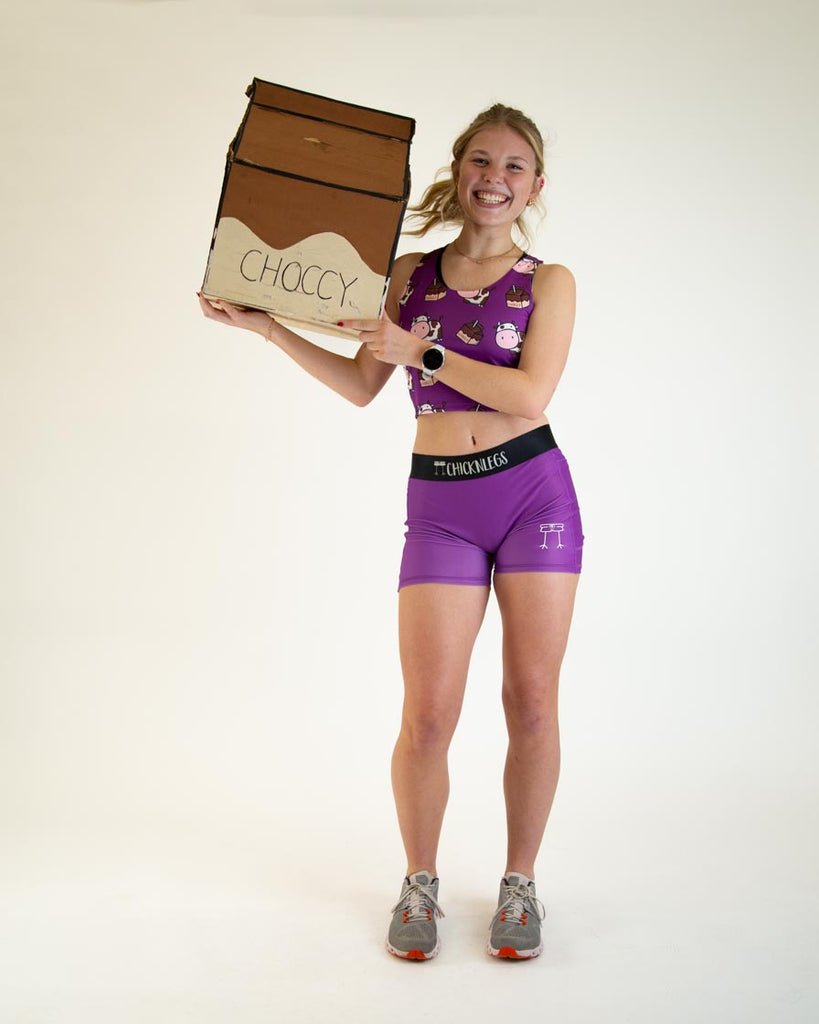 Runner is wearing ChicknLegs in the women's 3 in compression spandex with pockets for shorts in the solid deep purple design posing with the chocolate milk carton to match with the choccy cows.