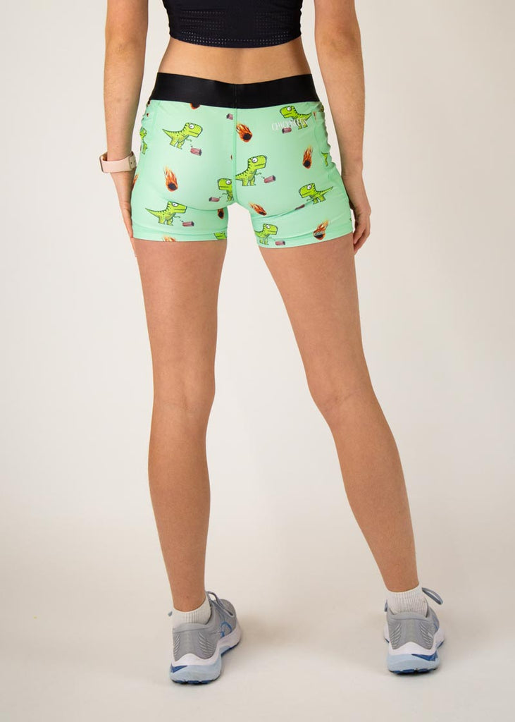 The model is a runner who is wearing Chicknlegs in women's 3" compression shorts, in the dino-sore design, facing away from the camera to show the back of the compression.