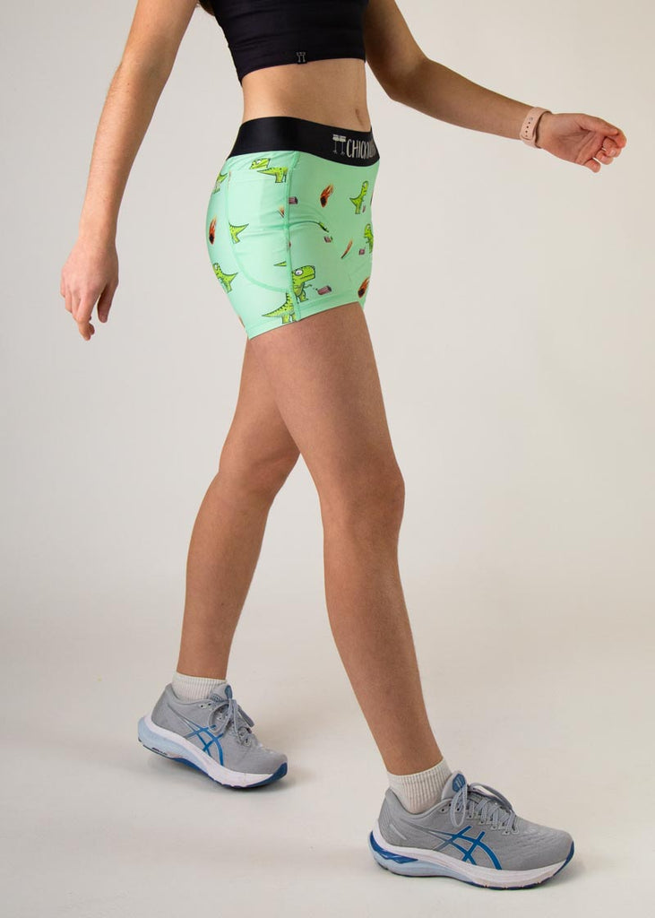 The model is a runner who is wearing Chicknlegs in women's 3" compression shorts, in the dino-sore design, facing right.
