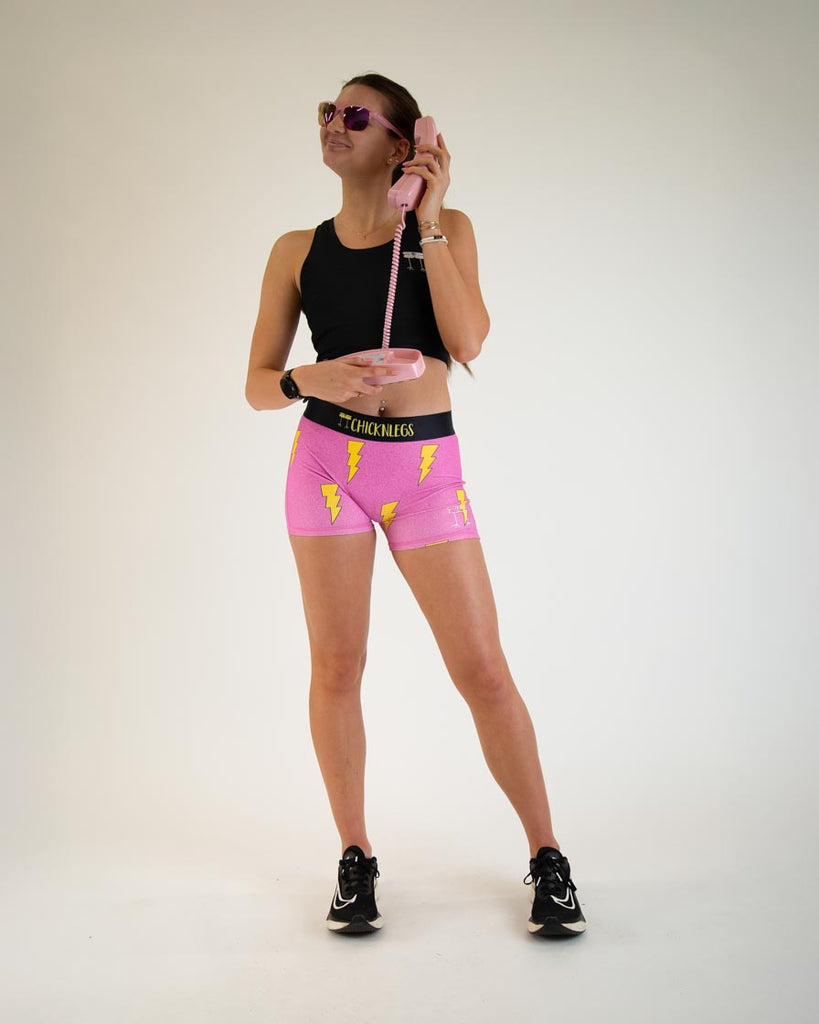 Runner is wearing ChicknLegs women's 3 in compression spandex with no pockets. The print is the hot pink bolts design. The model is posing holding a pink phone. Fast as speed!