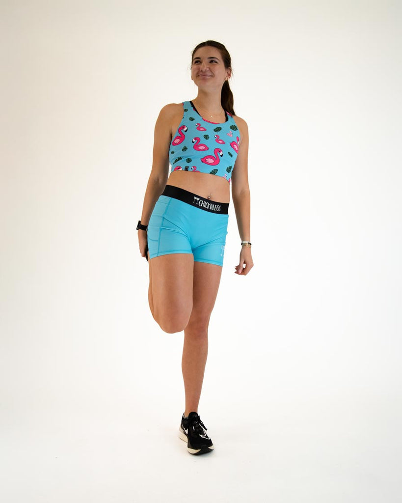 Runner is wearing ChicknLegs in the women's 3 in compression spandex shorts in the solid sky blue print. Posing while stretching their legs.