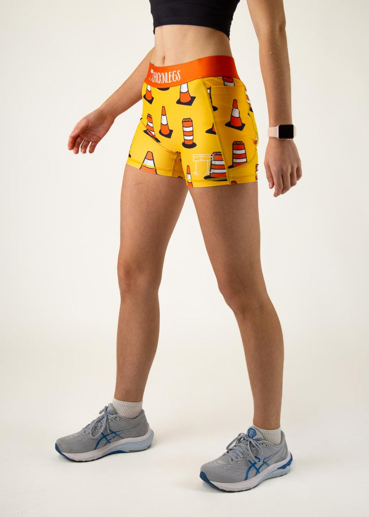 The model is a runner who is wearing Chicknlegs in women's 3" compression shorts in the traffic cones design, facing left.