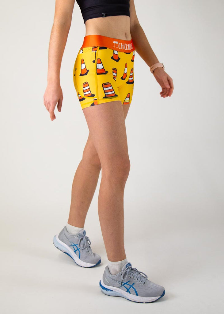 The model is a runner who is wearing Chicknlegs in women's 3" compression shorts in the traffic cones design, facing right.