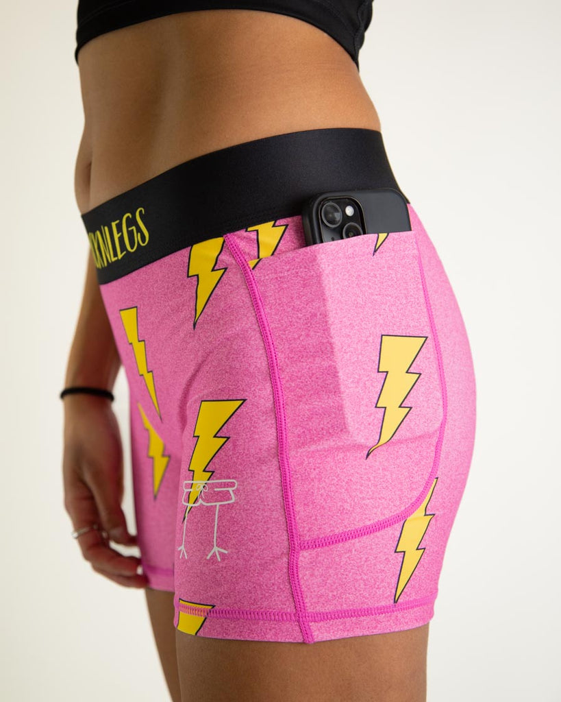 Runner is wearing ChicknLegs in the women's 3 in compression spandex with pockets shorts in the hot pink bolts design. The print has yellow lightning bolts on it with a hot neon pink background. The image is a close up of having a phone in the pocket, android or apple phone.