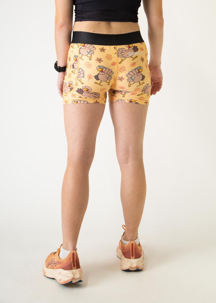 The model is a runner who is wearing Chicknlegs women's 3 inch compression shorts in the pardoned turkey design, facing away from the camera to show the back of the compression shorts.