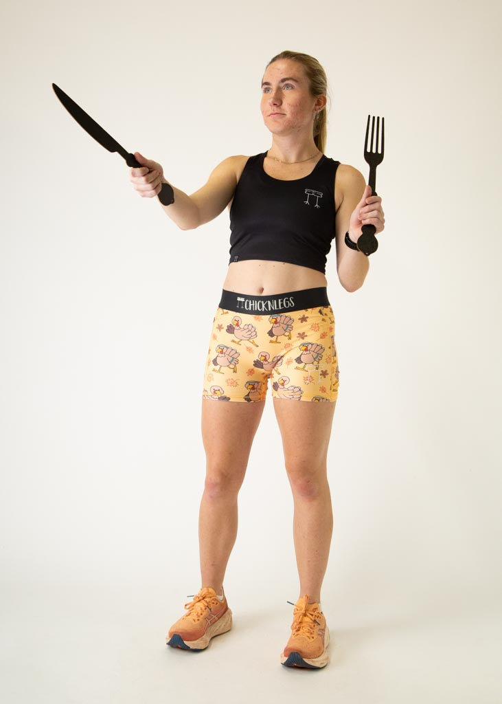The model is a runner who is wearing Chicknlegs women's 3 inch compression shorts in the pardoned turkey design, posing with a fork and a knife.