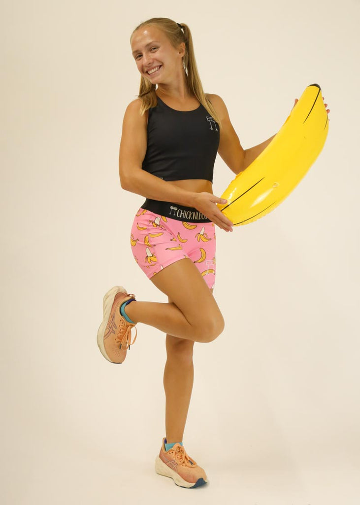 Model wearing Chicknlegs women's 3 inch compression shorts in the pink banana design posing with a banana.