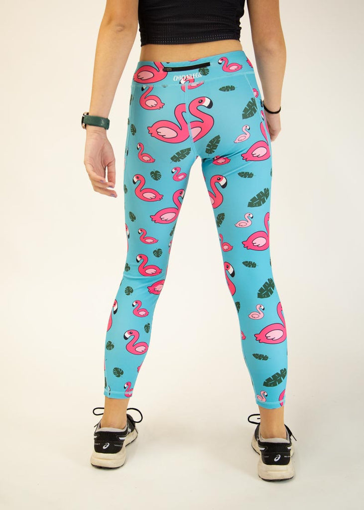 The model is a runner who is wearing Chicknlegs Women's Leggings in the Blue Flamingo design. These leggings include side pockets and an adjustable drawstring at the front. The model is facing away from the camera to show the back of the leggings.