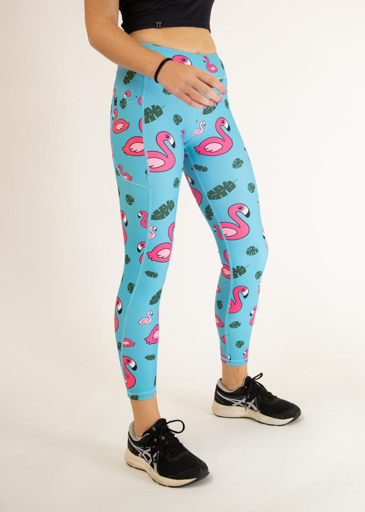 The model is a runner who is wearing Chicknlegs Women's Leggings in the Blue Flamingo design. These leggings include side pockets and an adjustable drawstring at the front. The model is facing slightly right.