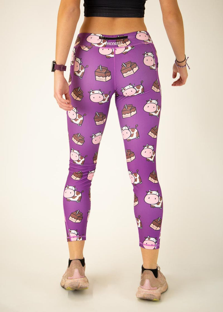The model is a runner who is wearing Chicknlegs Women's Leggings in the Choccy Cow design. These leggings include side pockets and an adjustable drawstring at the front. The model is facing away from the camera to show the back of the leggings.
