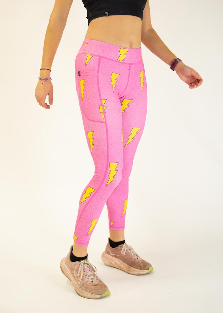 The model is a runner who is wearing Chicknlegs Women's Leggings in the Hot Pink Bolts design. These leggings include side pockets and an adjustable drawstring at the front. The model is facing slightly right to show the side.