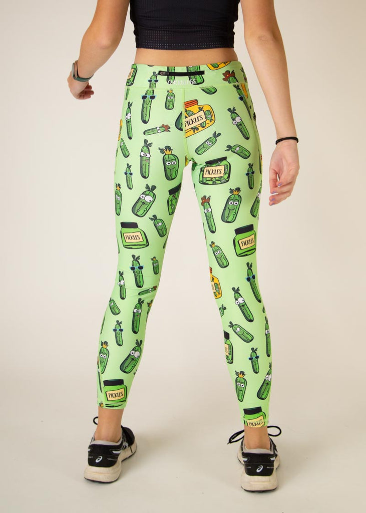 The model is a runner who is wearing Chicknlegs Women's Leggings in the Pickles design. These leggings include side pockets and an adjustable drawstring at the front. The model is facing away from the camera to show the back of the leggings.