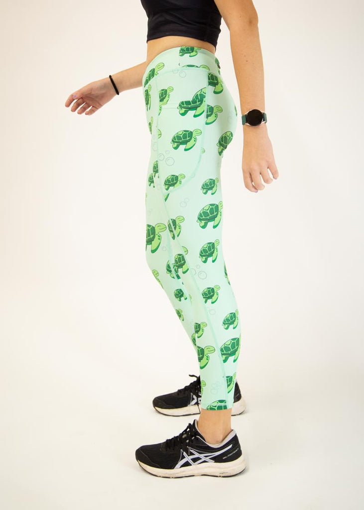 The model is a runner who is wearing Chicknlegs Women's Leggings in the Sea Turtles design. These leggings include side pockets and an adjustable drawstring at the front. The model is facing left.