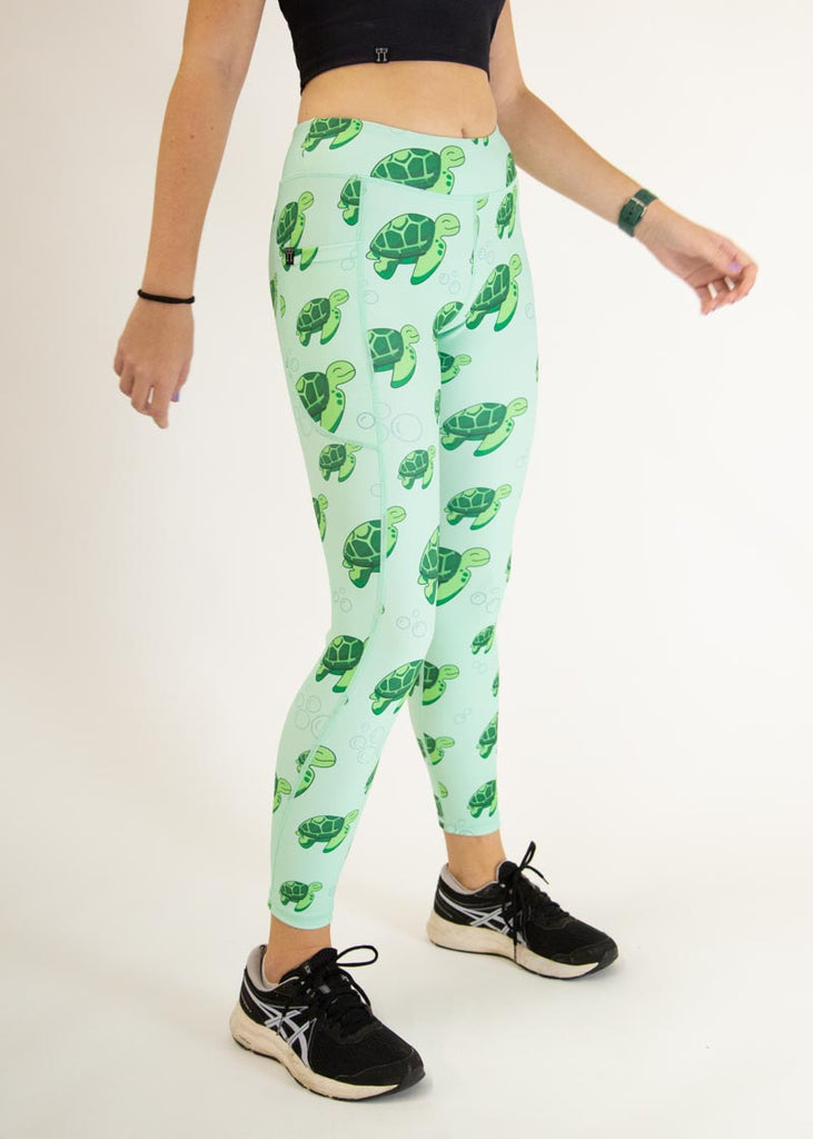The model is a runner who is wearing Chicknlegs Women's Leggings in the Sea Turtles design. These leggings include side pockets and an adjustable drawstring at the front. The model is facing slightly right to show the side.
