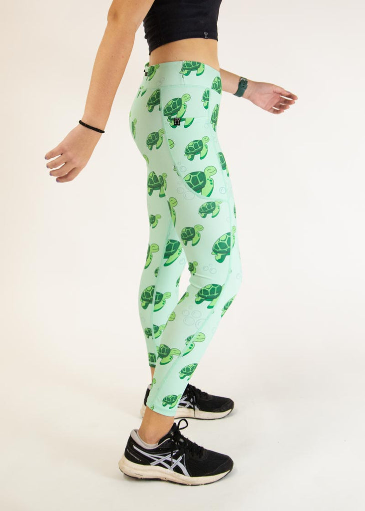 The model is a runner who is wearing Chicknlegs Women's Leggings in the Sea Turtles design. These leggings include side pockets and an adjustable drawstring at the front. The model is facing left to show the side of the leggings.