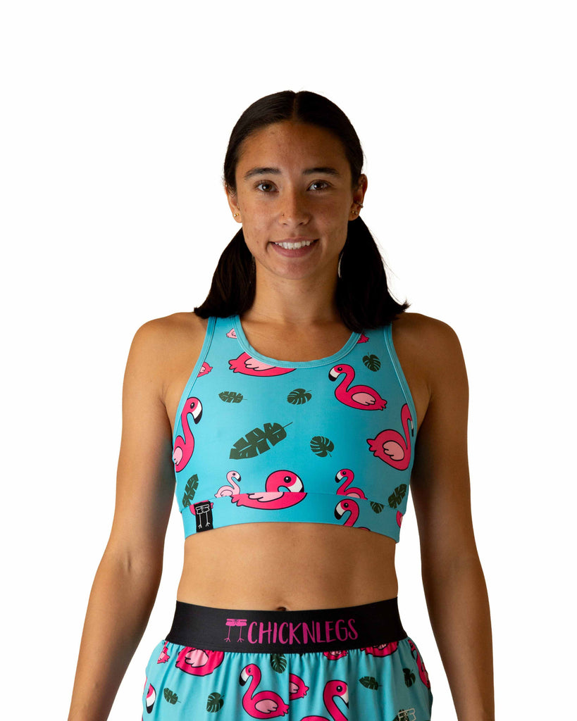 Runner is wearing ChicknLegs in the women's OG Sports Bra has a back pocket for exercise, running, workout, gym, and every day lifestyle. The print is the blue flamingo which has pink flamingos, green leaves and a blue background.