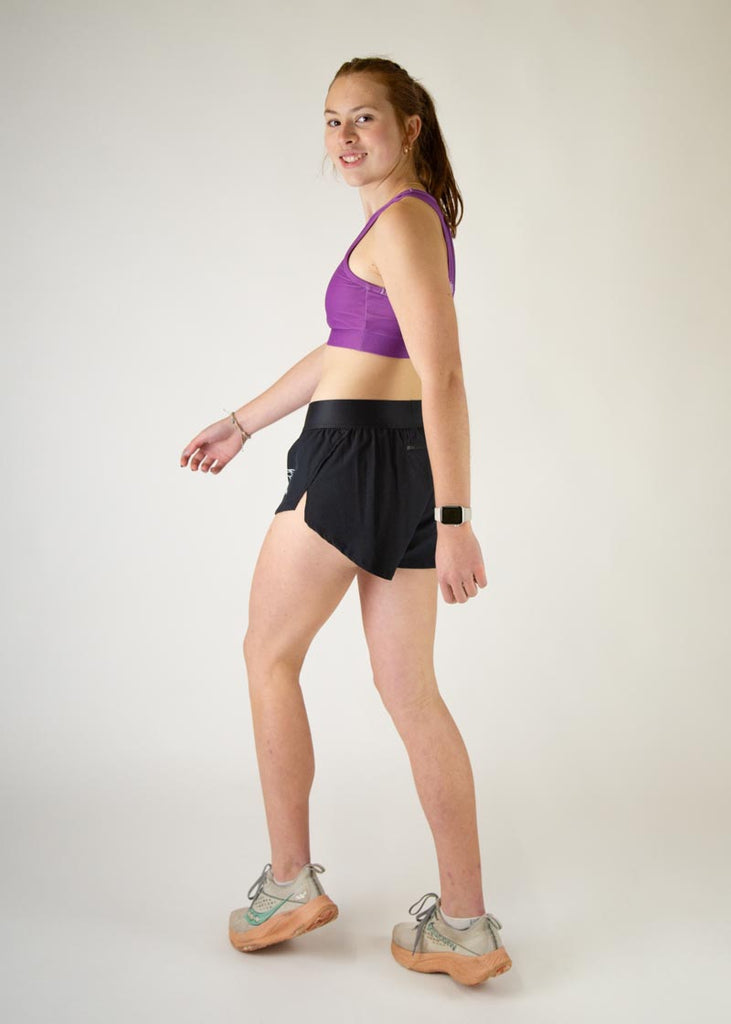 The model is a runner who is wearing Chicknlegs in thhe women's OG sports bra in the deep purple design, facing left while in a walking stance, a full body is shown.