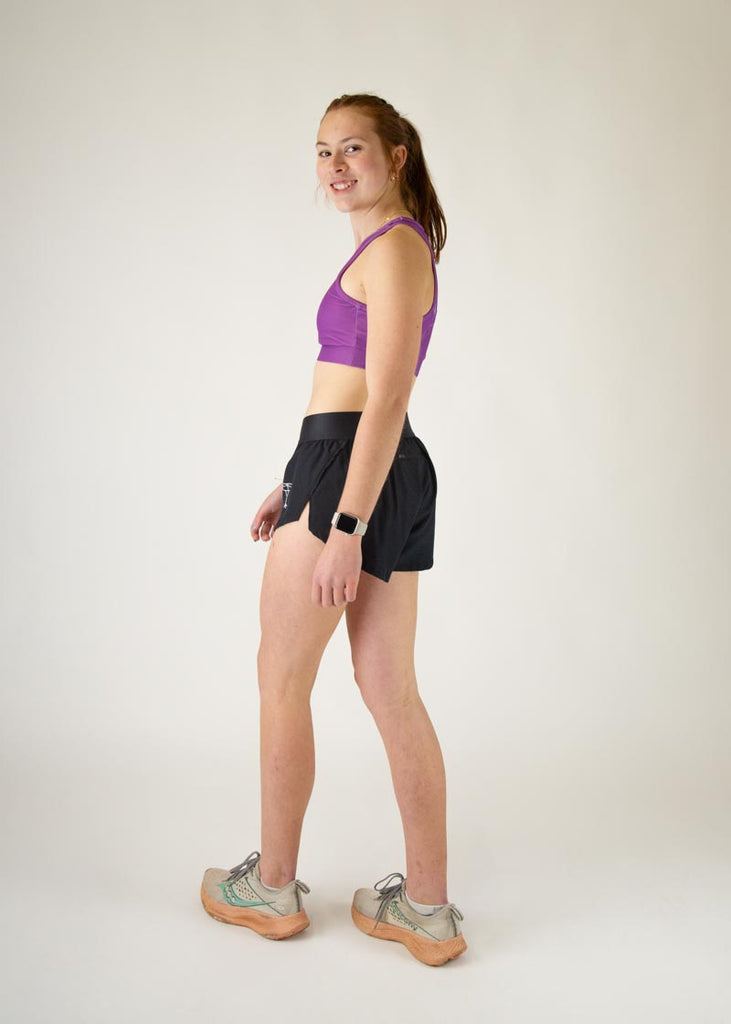 The model is a runner who is wearing Chicknlegs in thhe women's OG sports bra in the deep purple design, facing left while in a walking stance, a full body is shown.