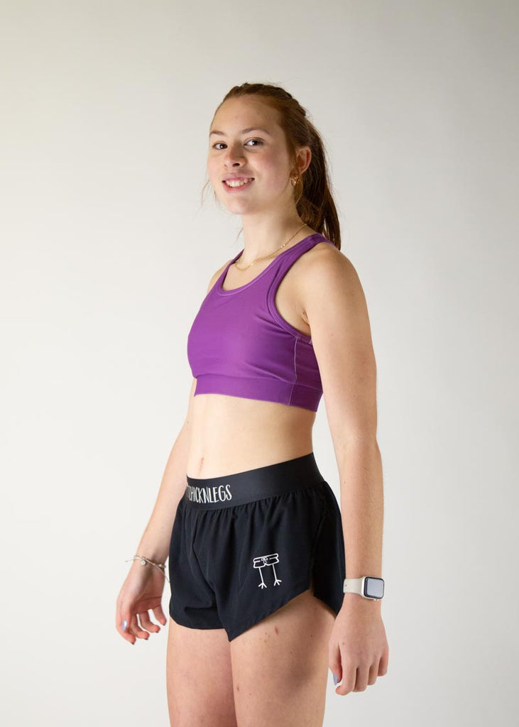 The model is a runner who is wearing Chicknlegs in thhe women's OG sports bra in the deep purple design, facing left.