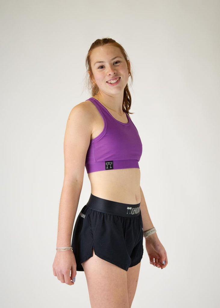 The model is a runner who is wearing Chicknlegs in thhe women's OG sports bra in the deep purple design, facing right.