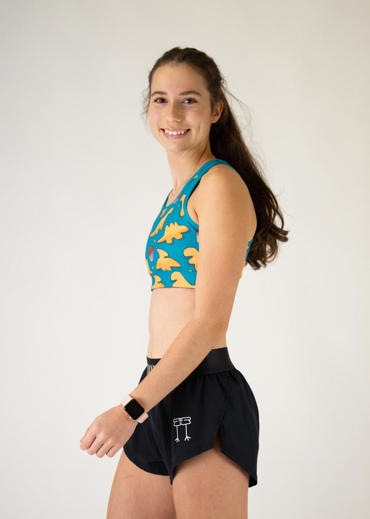 The model is a runner who is wearing Chicknlegs in the OG sports bra, in the dino nuggets design, facing left.