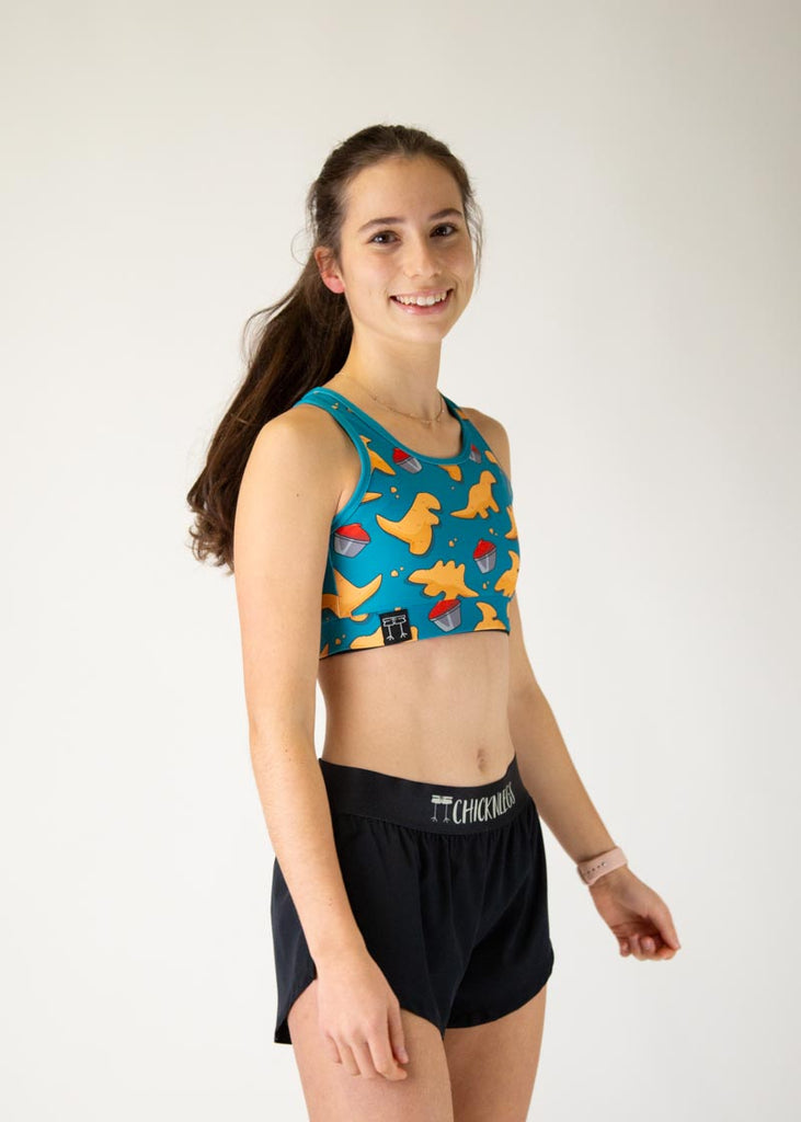 The model is a runner who is wearing Chicknlegs in the OG sports bra, in the dino nuggets design, facing right.