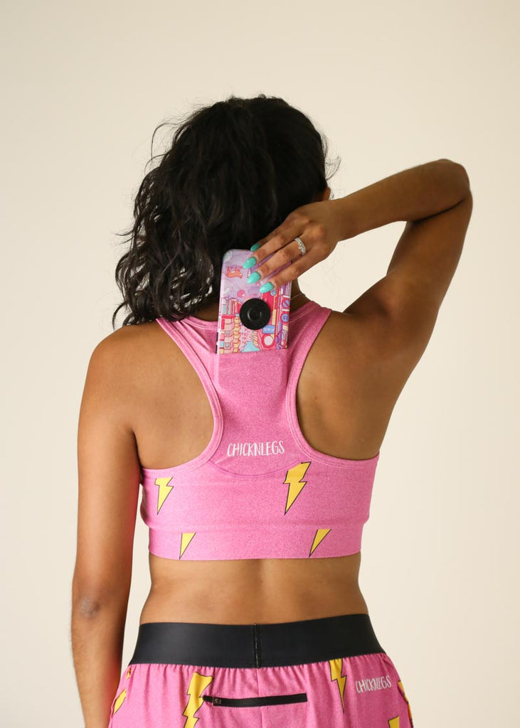 Back view of runner putting her phone into the pink bolts OG sports bra phone pocket.