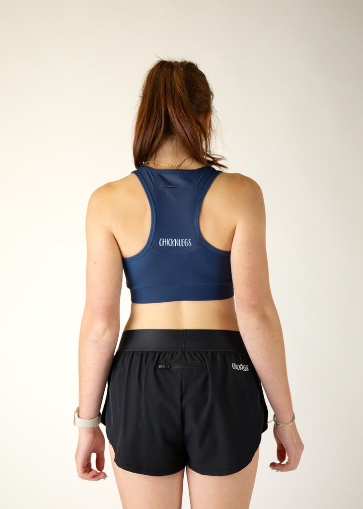 The model is a runner who is wearing Chicknlegs in the women's OG sports bra in the navy design, facing away from the camera to show the back of the sports bra.