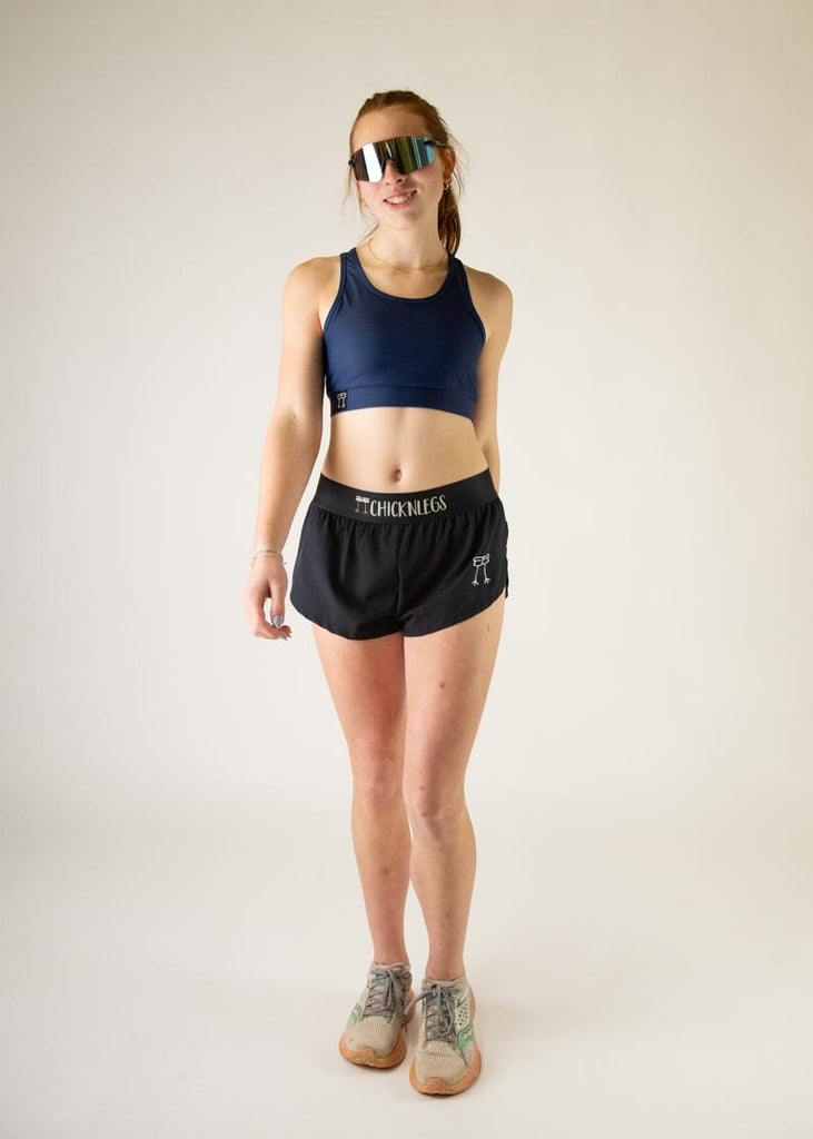 The model is a runner who is wearing Chicknlegs in the women's OG sports bra in the navy design, facing front while in a walking stance.