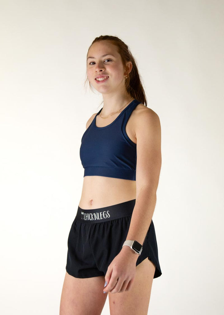The model is a runner who is wearing Chicknlegs in the women's OG sports bra in the navy design, facing left.