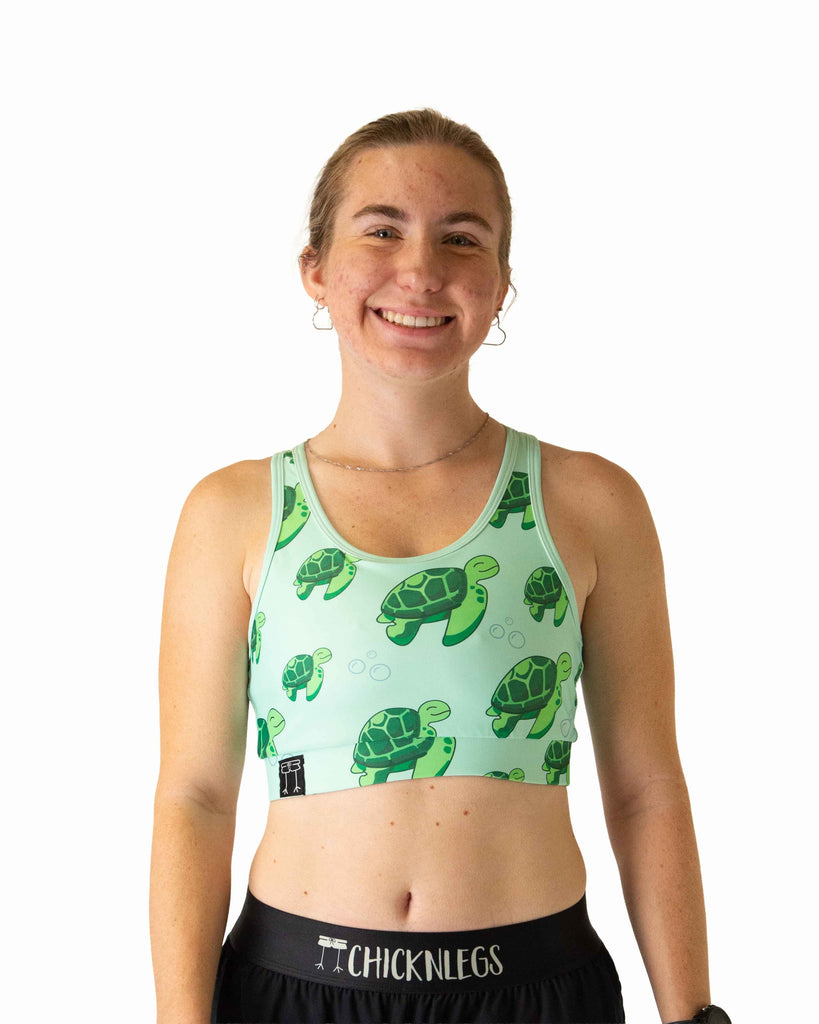 Runner is wearing ChicknLegs in the women's OG Sports Bra has a back pocket for exercise, running, workout, gym, and every day lifestyle. The print is the sea turtles design which has bubbles, green turtles on a light green background.