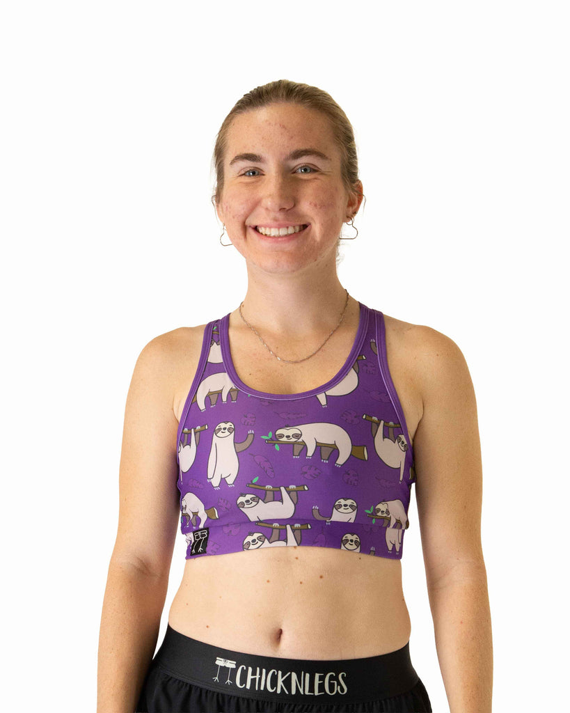 Runner is wearing ChicknLegs in the women's OG Sports Bra has a back pocket for exercise, running, workout, gym, and every day lifestyle. The print is the sloth design which has many sloths standing and sleeping with tree branches and leaves on a purple background.