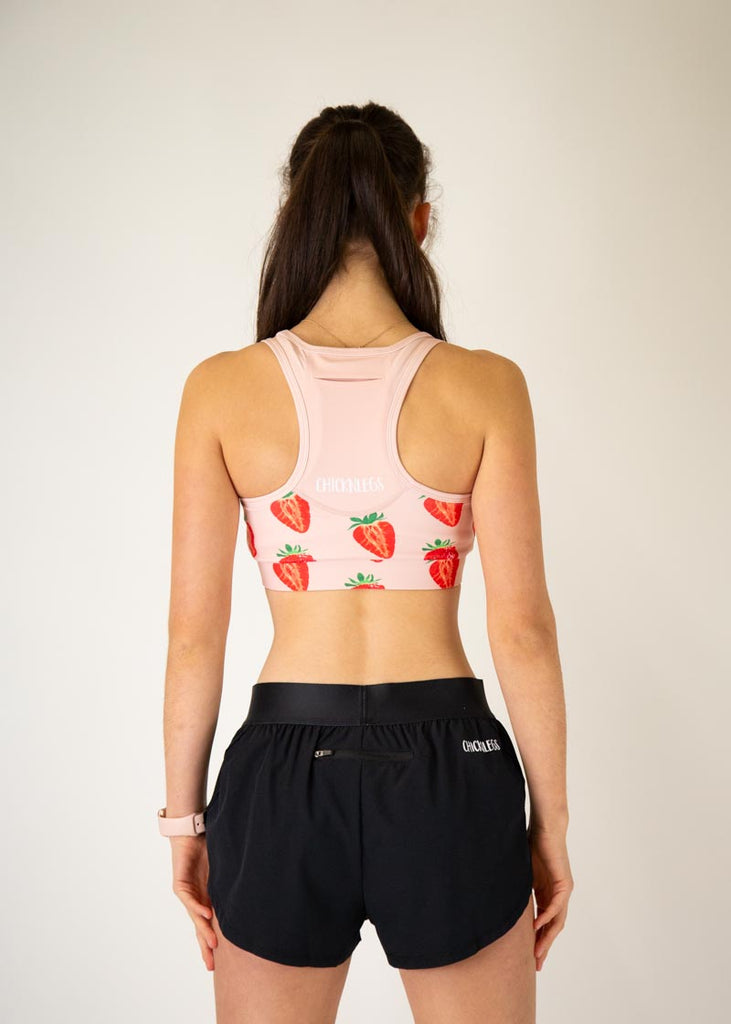 The model is a runner who is wearing Chicknlegs in the women's OG sports bra, in the strawberry SZN design, facing away from the camera to show the back of the sports bra.