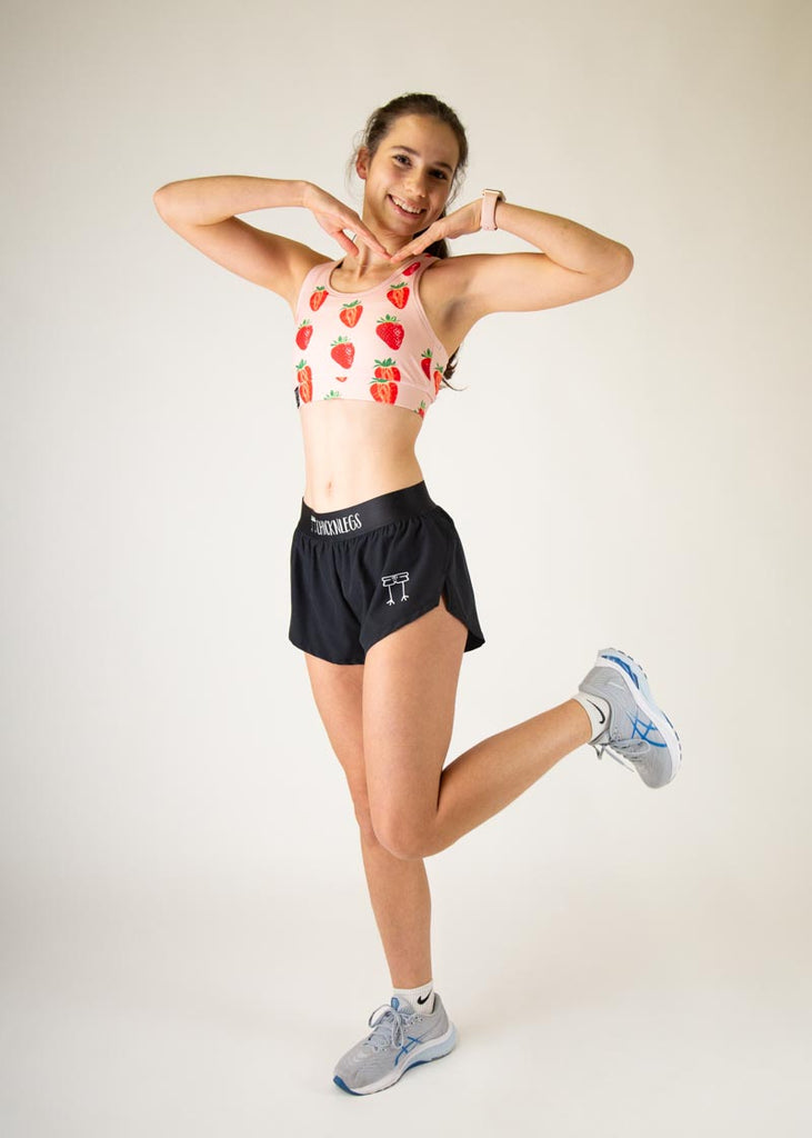 The model is a runner who is wearing Chicknlegs in the women's OG sports bra, in the strawberry SZN design, facing front while posing with their hands on their face. A full body photo is shown of the model.
