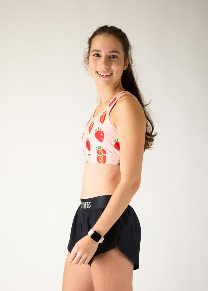 The model is a runner who is wearing Chicknlegs in the women's OG sports bra, in the strawberry SZN design, facing left.