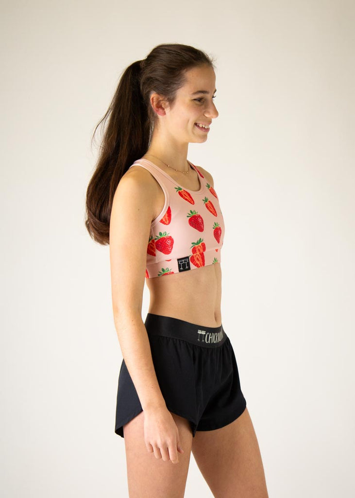 The model is a runner who is wearing Chicknlegs in the women's OG sports bra, in the strawberry SZN design, facing right.
