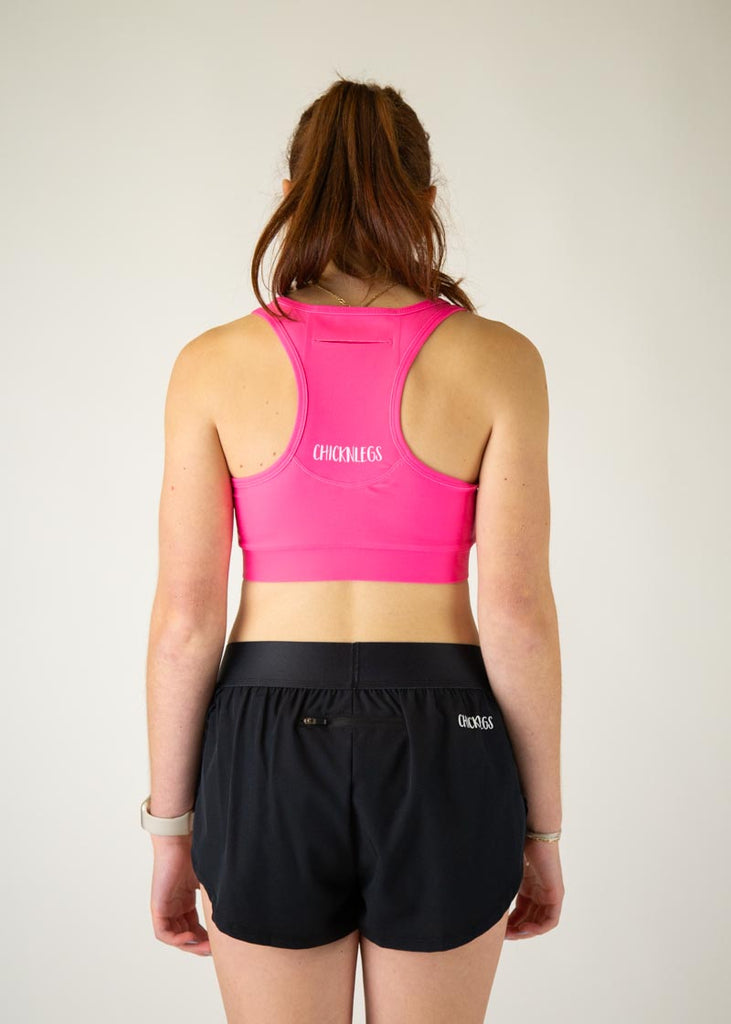The model is a runner who is wearing Chicknlegs in the women's OG sports bra in the neon pink design, facing away from the camera to show the back of the sports bra.